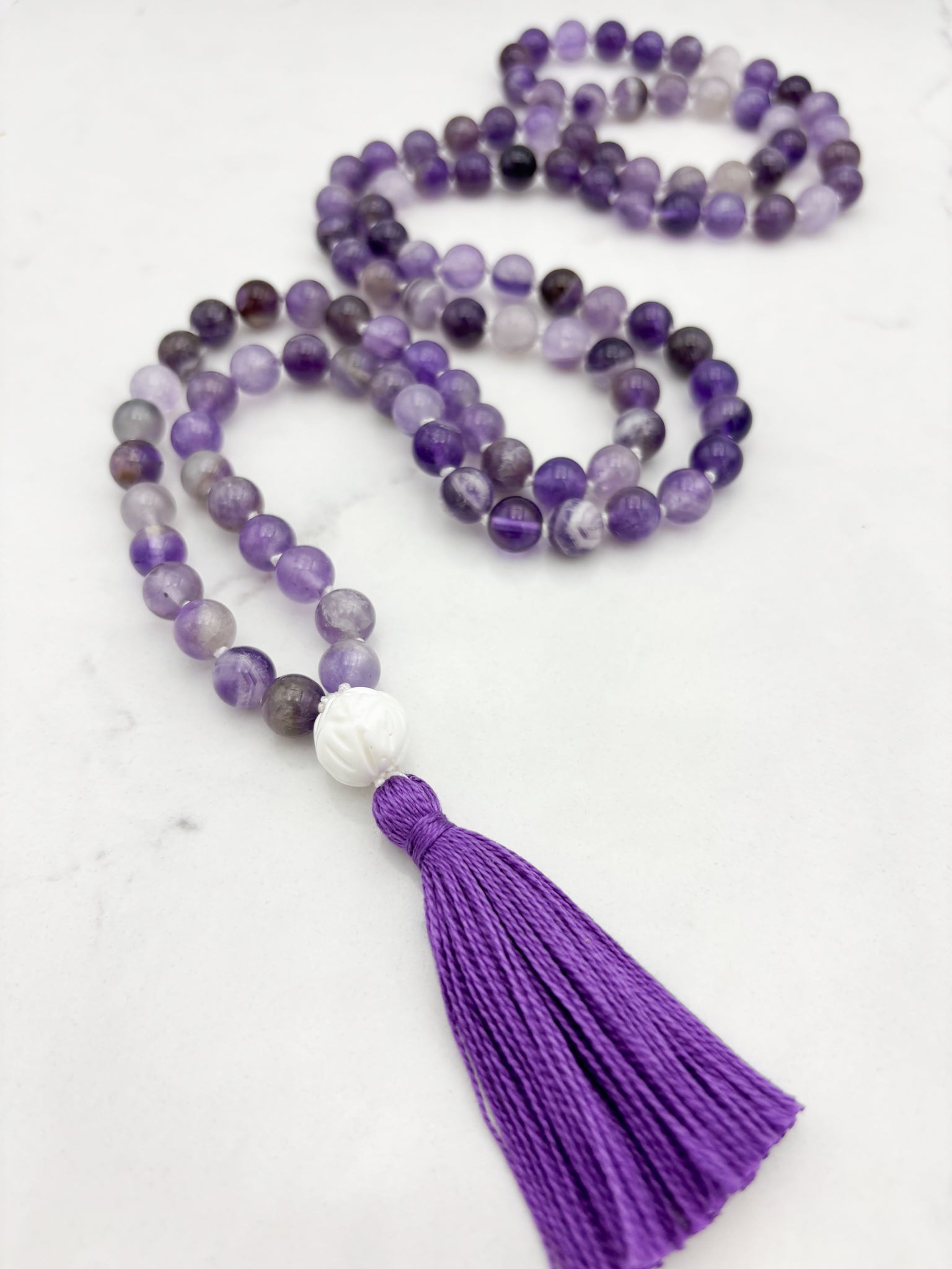 amethyst gemstone mala with carved tridacna shell guru bead and purple tassel | radiant malas | handmade in boulder, colorado